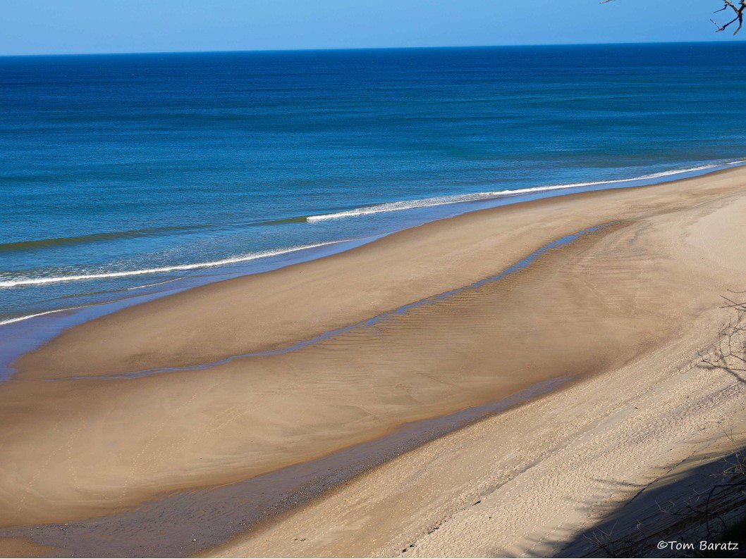 overhead view of sandy beach and blue ocean with sky in the background