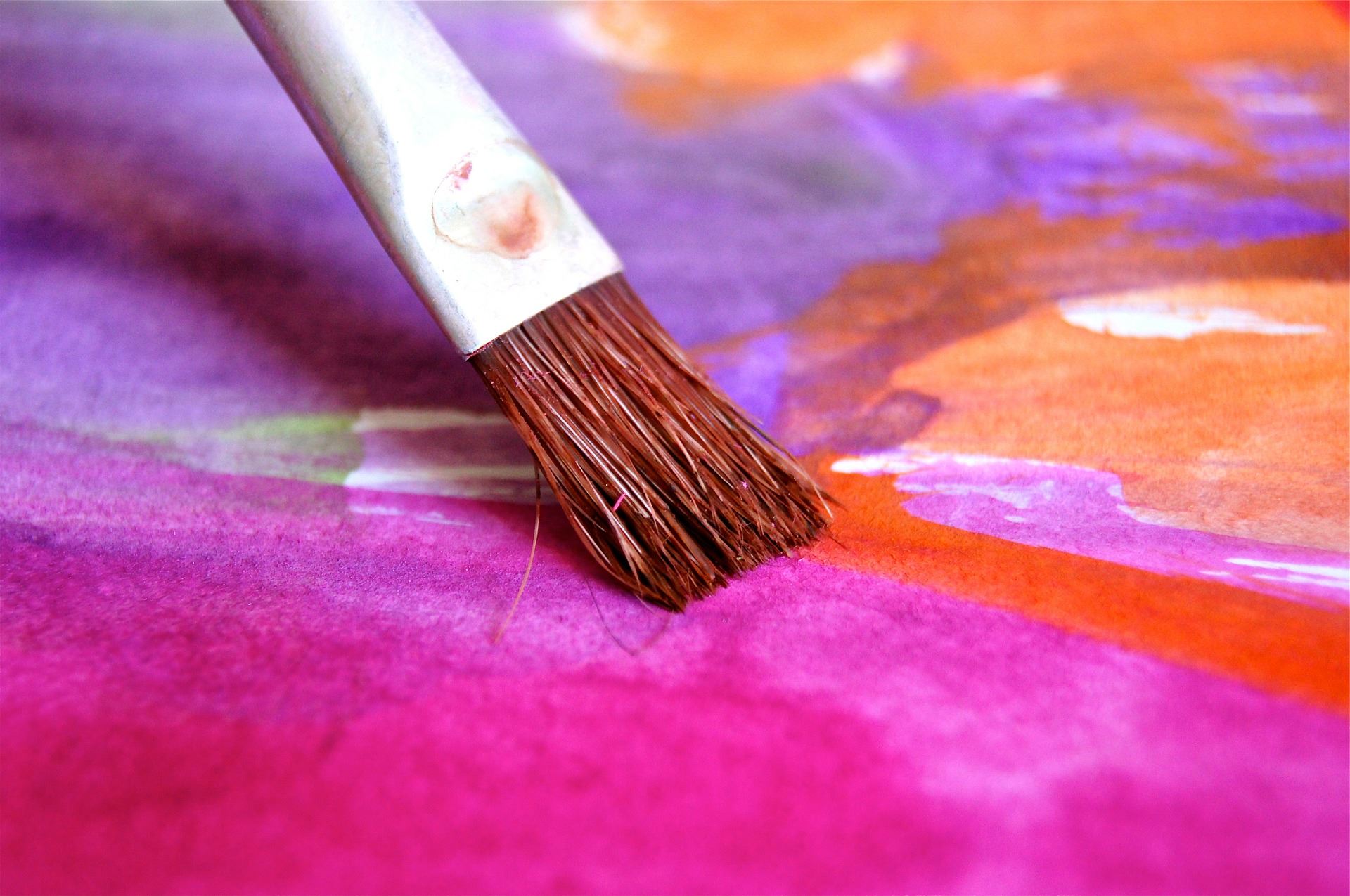 paintbrush on brightly colored pink and orange watercolor painting