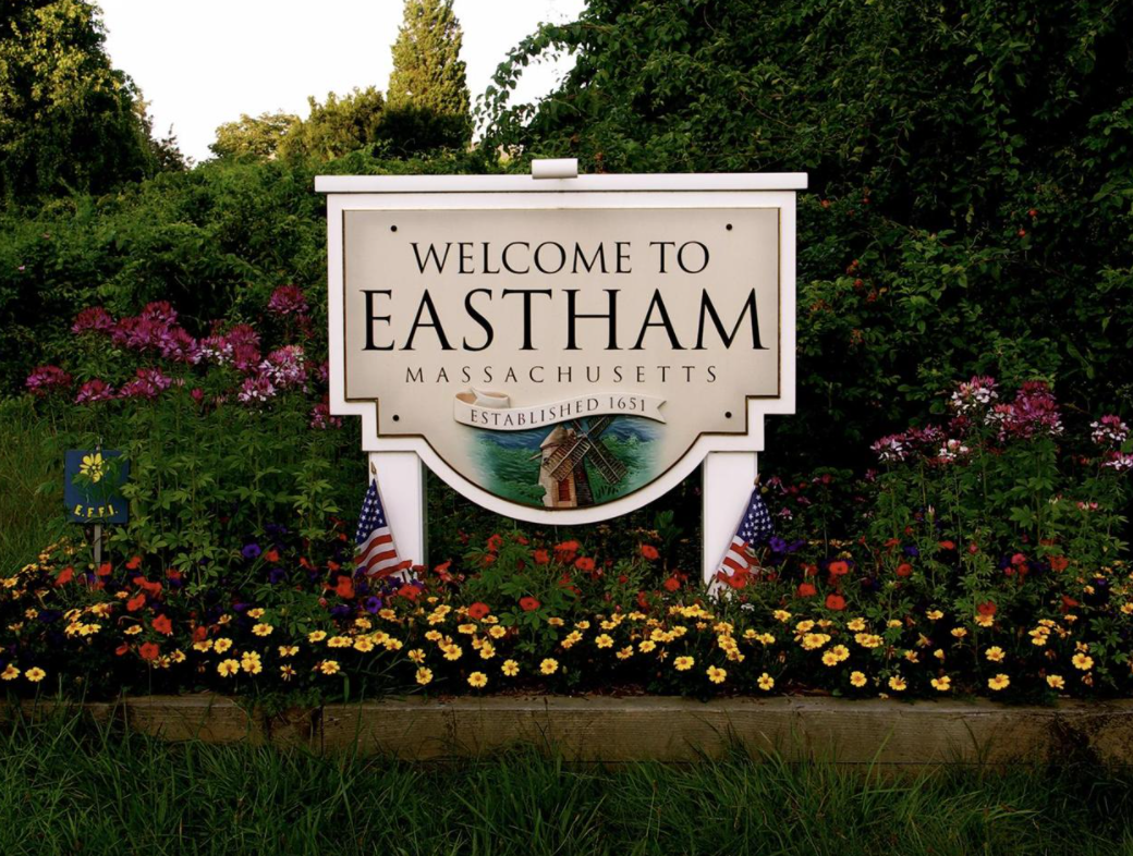 wooden sign reading welcome to Eastham with flowers and green grass around it